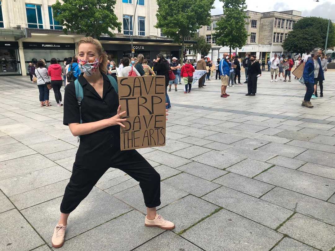 A young female holding a sign, saying save the TRP, save the arts.